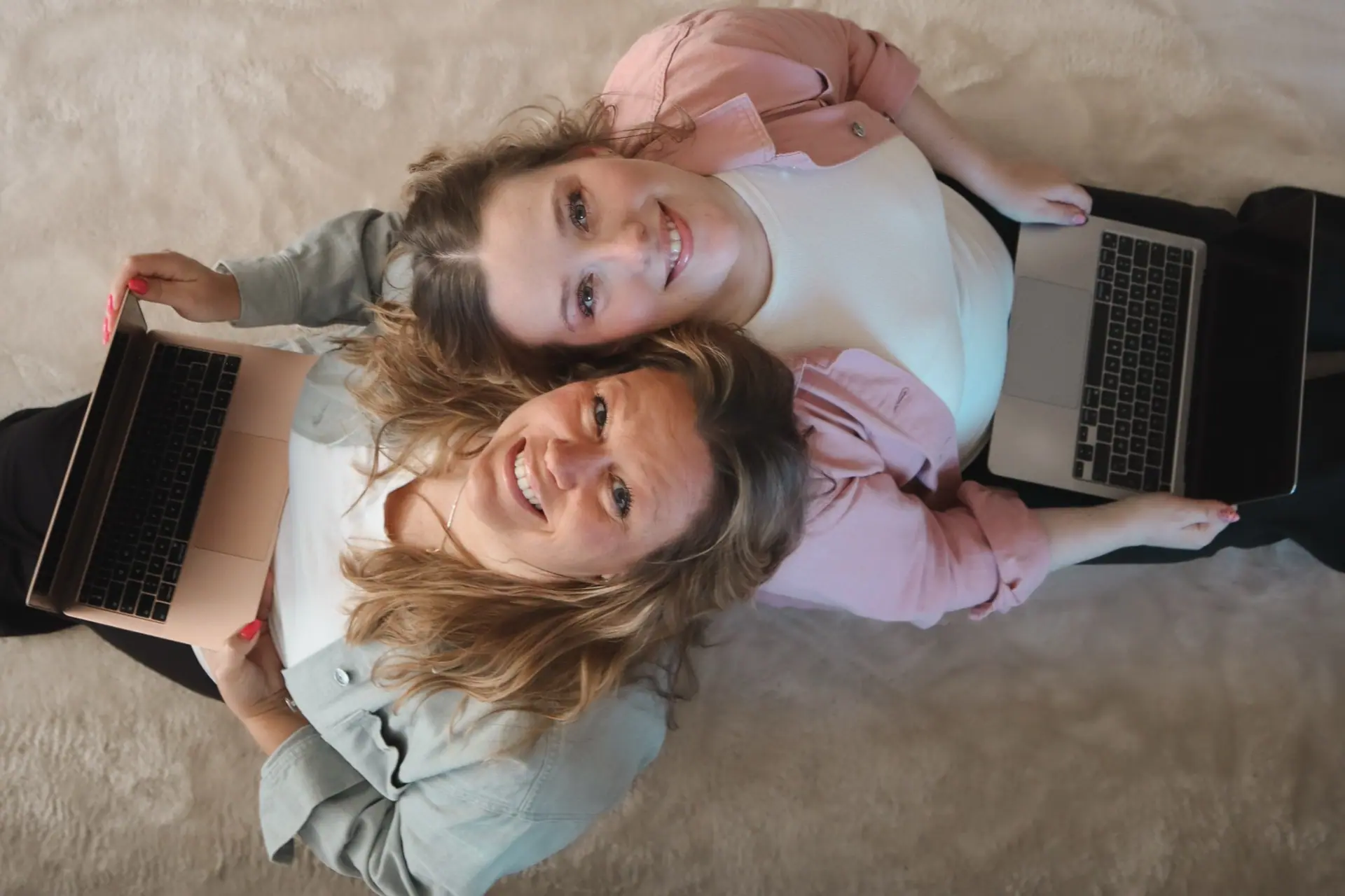 Amalie og Laila ligger på gulvet med hver sin laptop og kigger op